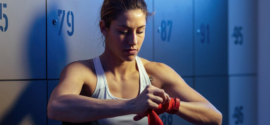 giovane donna atletica che si prepara per l'allenamento di boxe avvolgendo le mani con delle cinghie nello spogliatoio della palestra