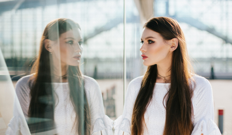 schöne Frau mit langen Haaren schaut ihr Spiegelbild in einem modernen Glasgebäude
