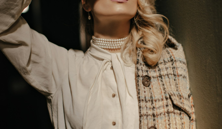 blonde lockige Frau Tweedjacke weiße elegante Bluse bedeckt Sonne mit Hand charmantes Mädchen schaut nach oben posiert dunklen Raum