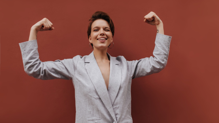 Exploring the Role of Confidence in Feminization 1 pretty lady suit showing her biceps brown background short haired woman grey stylish jacket demonstrates power isolated